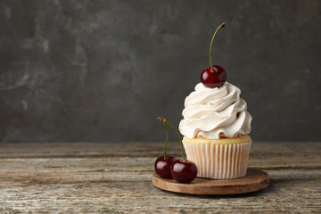 Delicious cupcake with cream and cherries on wooden table, space for text