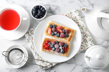 Tasty puff pastries with berries and tea on white marble table, flat lay