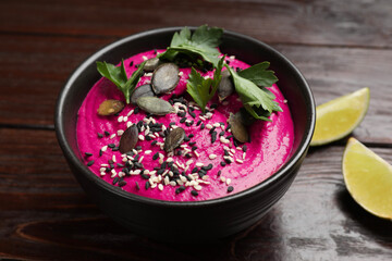 Tasty beetroot hummus, parsley and seeds in bowl on wooden table, closeup