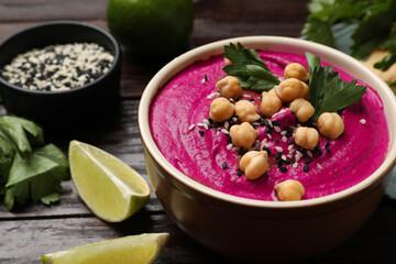 Tasty beetroot hummus in bowl and products on wooden table, closeup