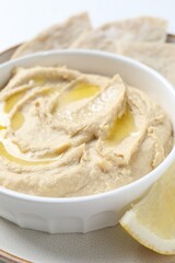 Delicious hummus with olive oil in bowl and lemon on white table, closeup