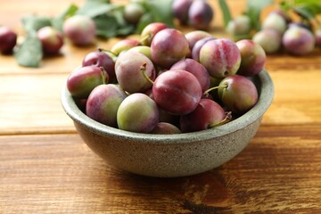 Ripe plums in bowl on wooden table, closeup