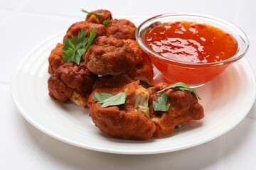 Baked cauliflower buffalo wings with parsley and sauce on white table, closeup