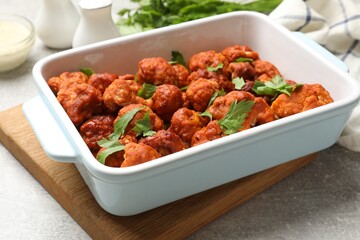 Fototapeta premium Baked cauliflower buffalo wings with parsley in baking dish on grey table, closeup