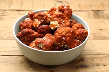 Tasty cauliflower buffalo wings in bowl on wooden table, closeup