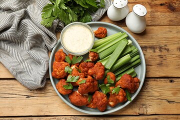 Tasty cauliflower buffalo wings, sauce and celery on wooden table, flat lay