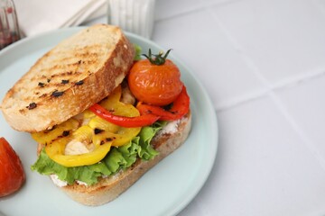 Tasty sandwich with grilled vegetables and cream cheese on white tiled table, closeup. Space for text