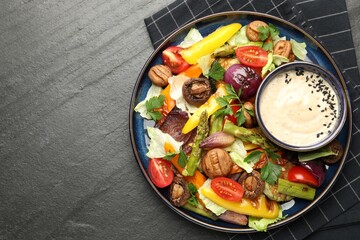 Delicious salad with grilled vegetables and sauce on dark gray textured table, top view. Space for text