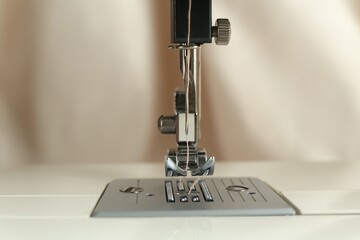 Sewing machine with beige thread on blurred background, closeup