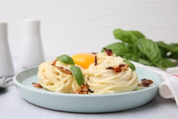 Delicious pasta Carbonara with egg yolk, bacon and basil on light gray table, closeup