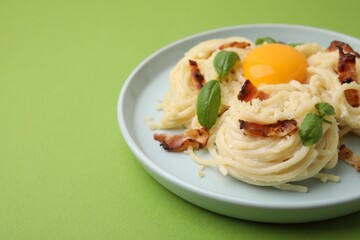 Delicious pasta Carbonara with egg yolk, bacon and basil on green table, closeup. Space for text