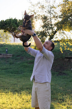 Smiling middle-aged man walks and plays with a small dog in public park