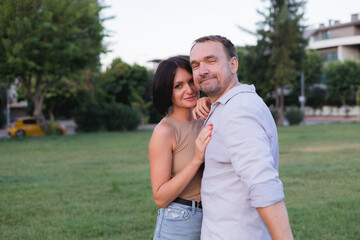 A happy smiling couple walking, hugging and kissing in park on late summer sunset
