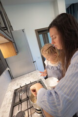 Mother and a small daughter cooking food at home in the kitchen