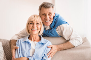 Lovely mature man embracing wife and smiling together to camera, resting at home