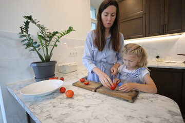 Mother and a small daughter cooking food at home in the kitchen