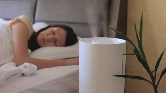 Home humidifier diffusing water while woman sleeping on bed. 
