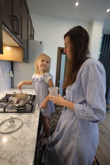 Mother and a small daughter cooking food at home in the kitchen