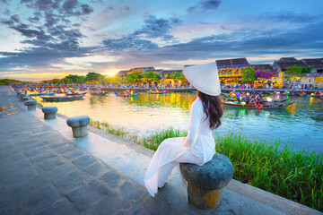 Vietnamese woman in national costume enjoying beautiful evening view of ancient town, Hoi An, Vietnam, business and tourism and trade transportation with traditional boats decorated with paper lantern