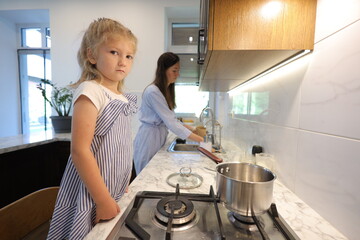 Mother and a small daughter cooking food at home in the kitchen