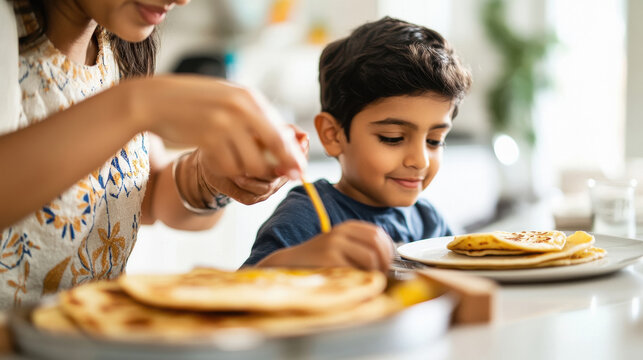 a mother adding ghee on the roti, son sitting on the table with his plate kept in front of him - Powered by Adobe