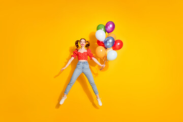 Photo of young red hair funky positive girl wearing blouse and jeans flying helium air balloons entertainment isolated on yellow color background