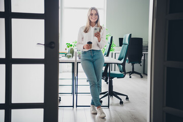 Full size photo of nice elegant young woman drink coffee use phone wear shirt modern office building indoors