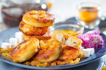 Fried cottage cheese pancakes syrniki with raisins and grapes on a blue dish served with black tea.