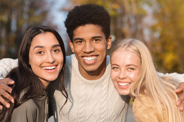 Obraz premium Portrait of three multiethnic friends guy and girls smiling over park background, close up