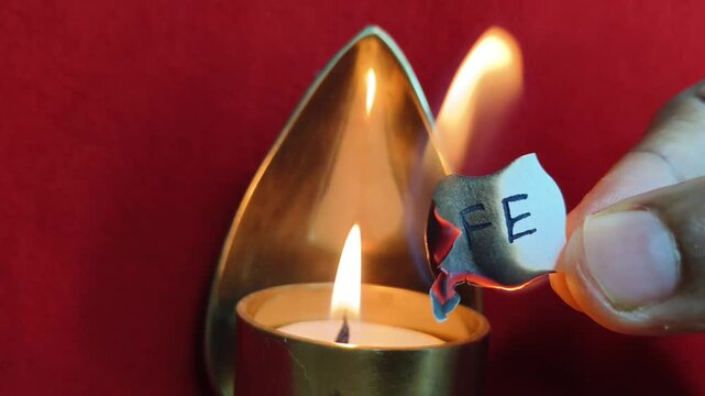 Hand holding white paper note with life word or text written on the surface and burning it on a wax candle fire flame isolated on a red background. Bad life depression or wasting life symbolic concept