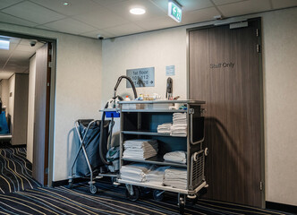 A side view of a hotel corridor shows cleaning tools belonging to a janitor, with first-floor signage and room numbers visible on the wall, indicating ongoing maintenance - staff only signage on door