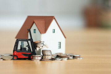 Construction house budget concept, with miniature house and forklift near piles of coins
