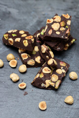 Pieces of dark chocolate with nuts on a gray background, top view, copy space. Homemade chocolate bar. Healthy eating concept. 