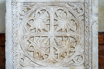 Ancient sarcophagus decoration with carved sculptures in stone representing a cross amidst floreal motifs