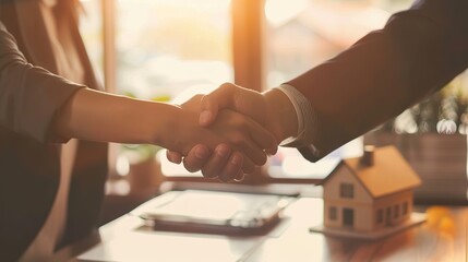 Professional real estate agent confidently shaking hands with a satisfied client over a desk with a house model and keys.real estate closing handshake,successful property deal