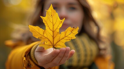 Woman holding a yellow leaf in her hands, wearing autumn clothes, with a blurred outdoor background. Concept of fall season and nature appreciation.