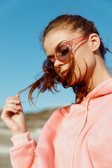 Stylish woman in pink sweatshirt and sunglasses enjoying beach breeze with hair blowing in wind