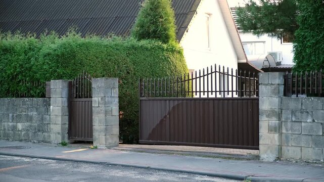 Closing of automatic entrance gate of brown color made of metal. Block fence. Entrance group for cars in the private house. Distance control. Smart home system