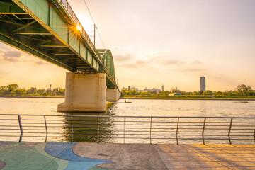 The sun sets behind Branko Bridge, casting golden light over the Sava River. The serene waters...