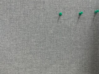 A gray fabric board with three green pushpins arranged on its surface, ready for office use.