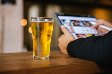 A close-up of a frothy, cold pint of golden beer in a transparent glass, set on a wooden table in a dimly lit pub, evoking a vintage, celebratory atmosphere.