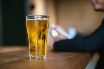 A man pours frothy beer into a glass at a lively pub. Friends gather around the bar, enjoying drinks and celebrating, with a warm, golden glow highlighting the joyful, friendly atmosphere.
