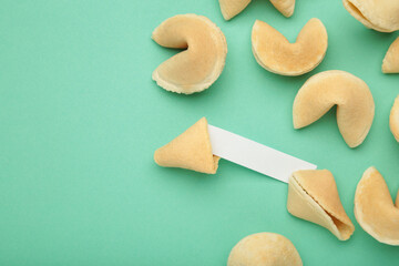 Tasty fortune cookies and paper with prediction on mint background. Top view