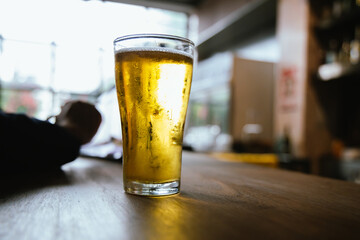 A man pours frothy beer into a glass at a lively pub. Friends gather around the bar, enjoying drinks and celebrating, with a warm, golden glow highlighting the joyful, friendly atmosphere.