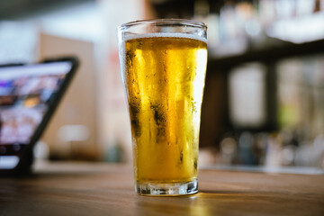 A man pours frothy beer into a glass at a lively pub. Friends gather around the bar, enjoying drinks and celebrating, with a warm, golden glow highlighting the joyful, friendly atmosphere.