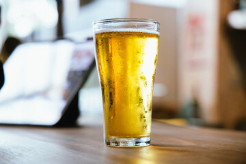 A man pours frothy beer into a glass at a lively pub. Friends gather around the bar, enjoying drinks and celebrating, with a warm, golden glow highlighting the joyful, friendly atmosphere.
