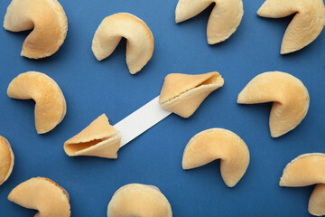 Tasty fortune cookies and paper with prediction on blue background. Top view