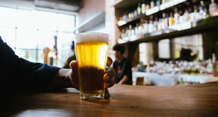 A man pours frothy beer into a glass at a lively pub. Friends gather around the bar, enjoying drinks and celebrating, with a warm, golden glow highlighting the joyful, friendly atmosphere.