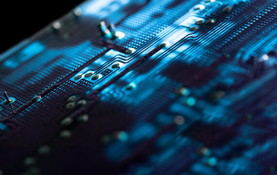 Close-up of an illuminated blue electronic circuit board with many electrical components, isolated on black background, selective focus