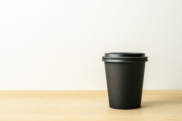 mockup black paper coffee cup, on a beige wooden table 